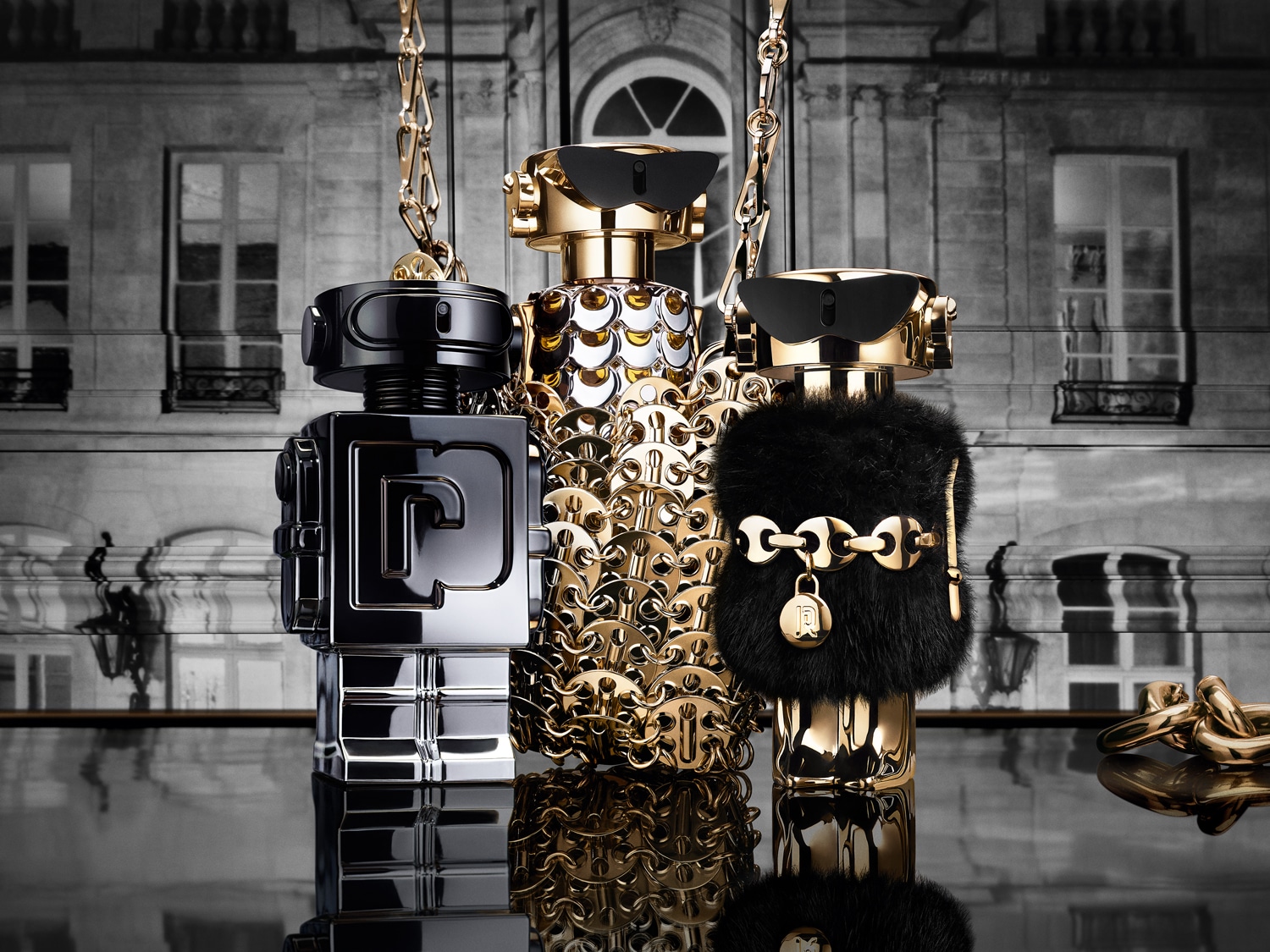 Három egyedi parfümös üveg látható: egy fekete, egy arany láncos és egy fekete szőrmés, mindegyik arany lánccal van díszítve, és egy épület háttere előtt állnak.