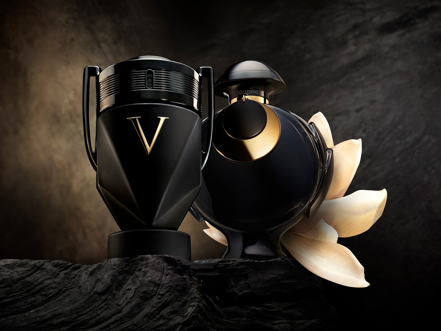 Két Paco Rabanne parfümös üveg látható: az egyik egy fekete trófea alakú üveg arany V betűvel, a másik egy fekete gömb alakú üveg, amelyet fehér szirmok vesznek körül.