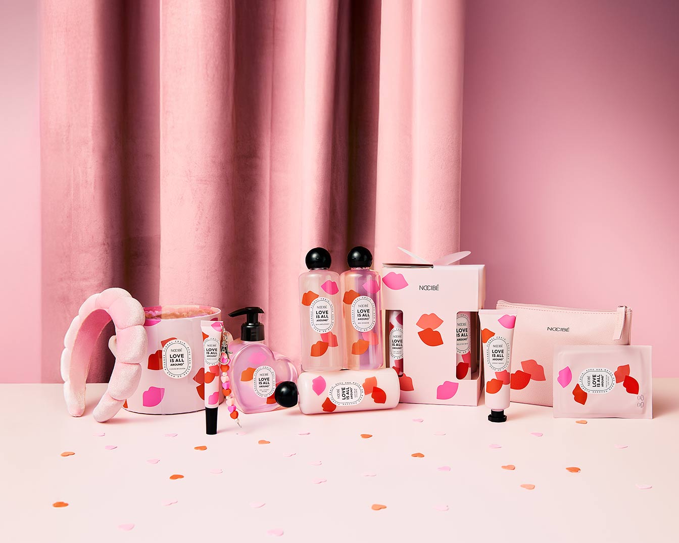 Découvrez un ensemble de produits de beauté Nocibé sur un fond rose doux, comprenant des lotions, des crèmes et des accessoires, tous ornés du motif « Love is All Around ».