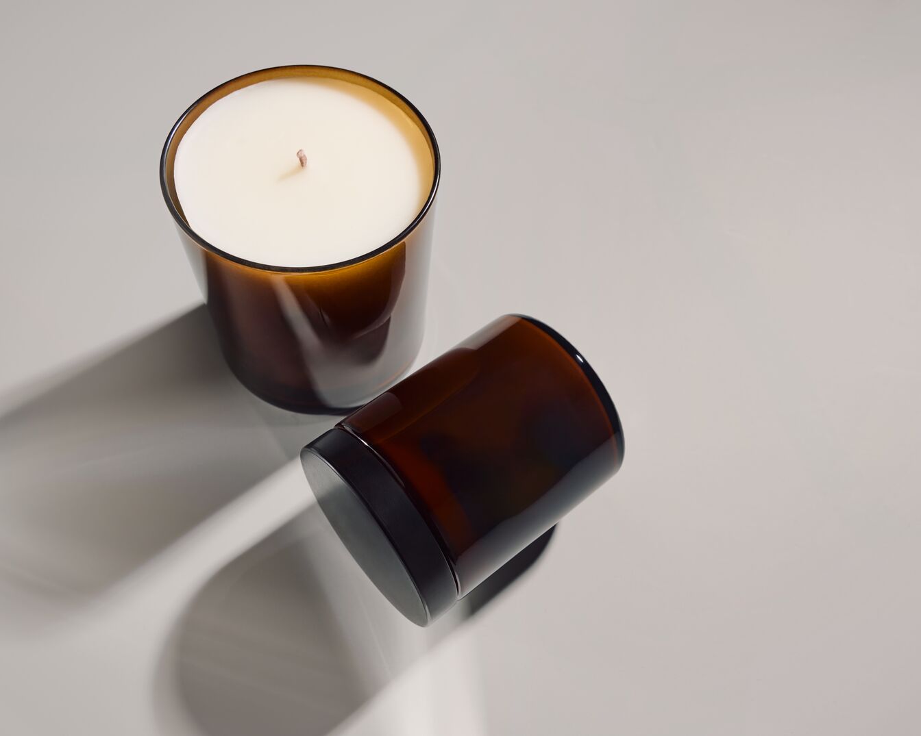 Twee bruine glazen kaarsen, waarvan één rechtop staat met witte was en een lont, en de andere ligt op zijn kant met een zwarte deksel.