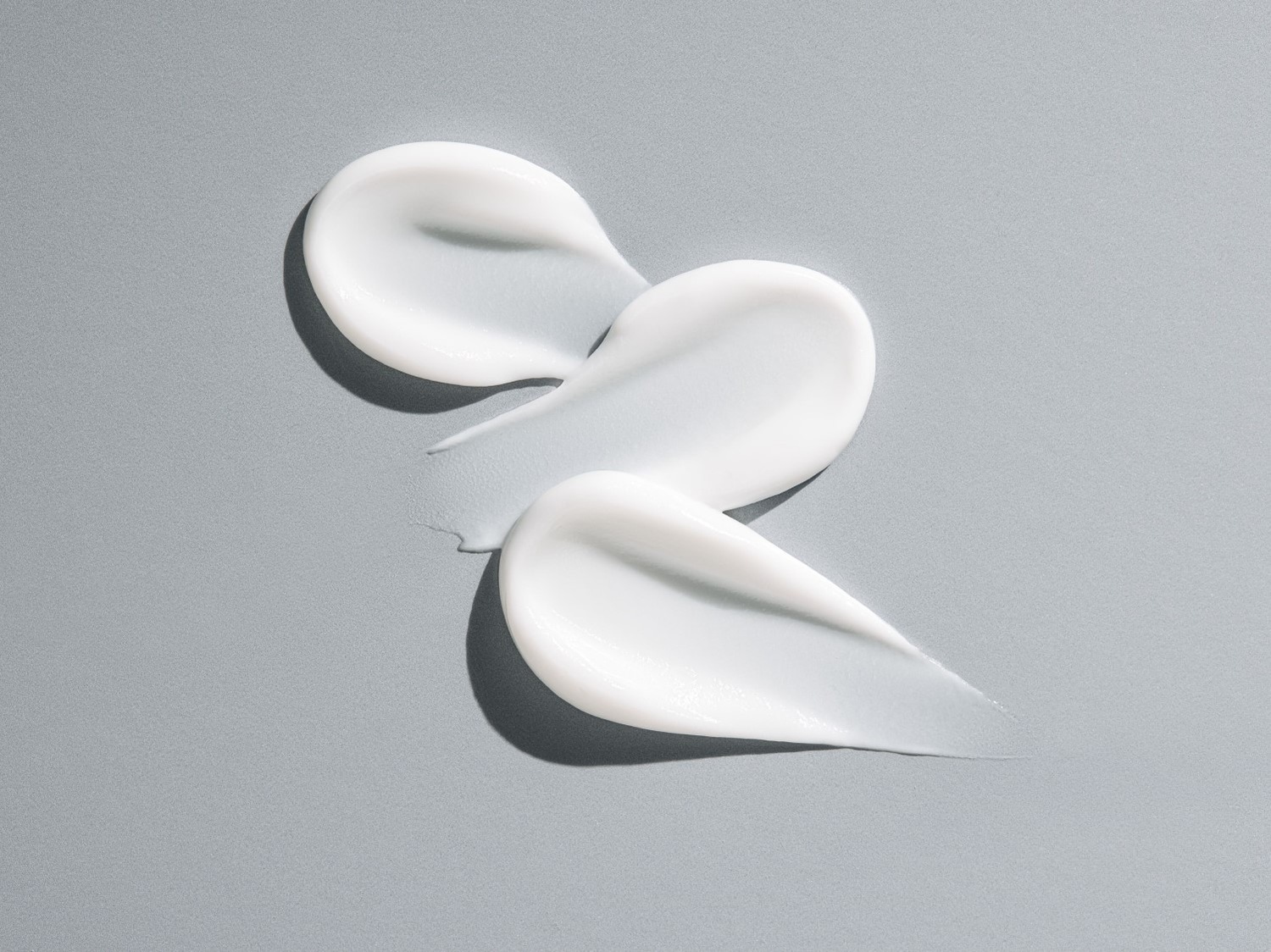 Drie vegen witte, dikke crème liggen op een grijze achtergrond, klaar om je huid te hydrateren en te verzorgen.