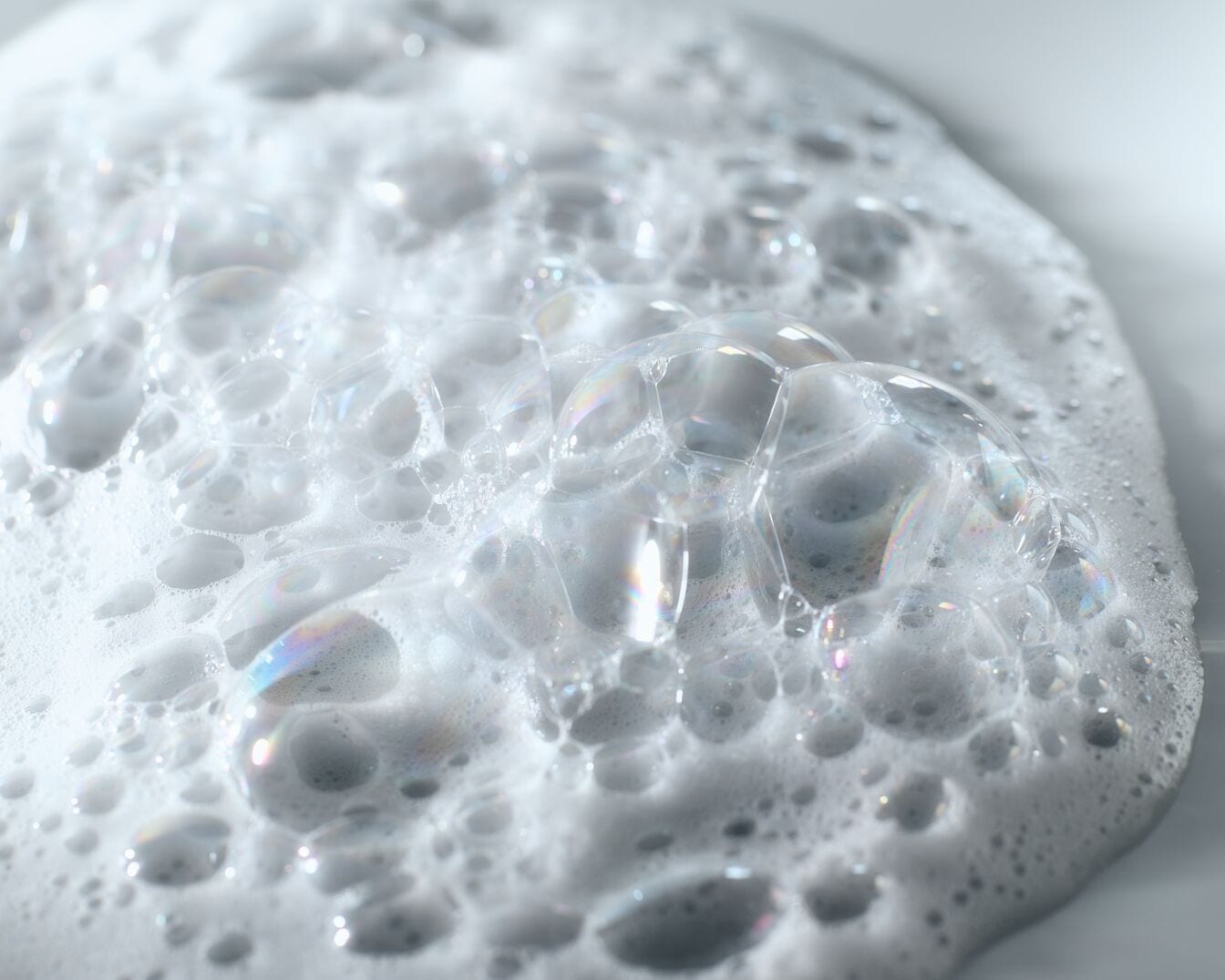 Nahaufnahme von schimmernden, irisierenden Blasen, die eine dichte, schaumige Textur bilden.