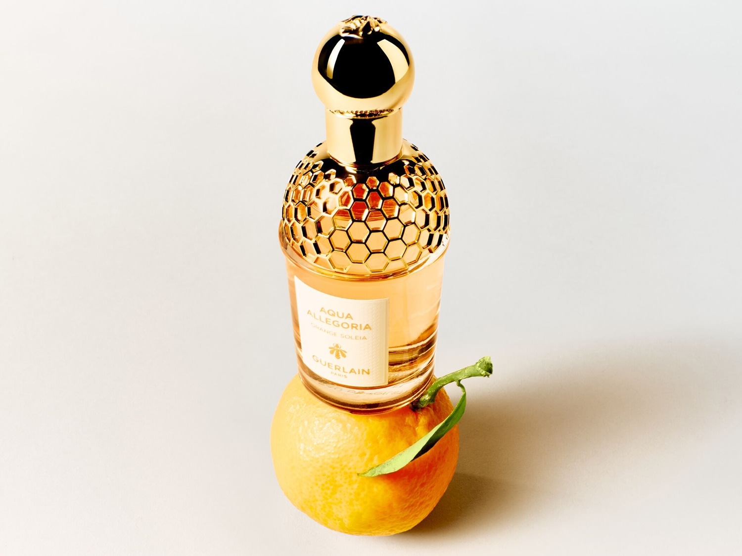 Ein Flakon Aqua Allegoria Orange Soleia von Guerlain mit goldenem Wabendeckel steht auf einer Orange.