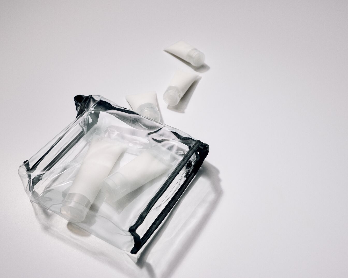 Transparente Kosmetiktasche mit schwarzen Akzenten und mehreren weißen Tuben, ideal für Reisen oder zur Aufbewahrung von Beauty-Produkten.