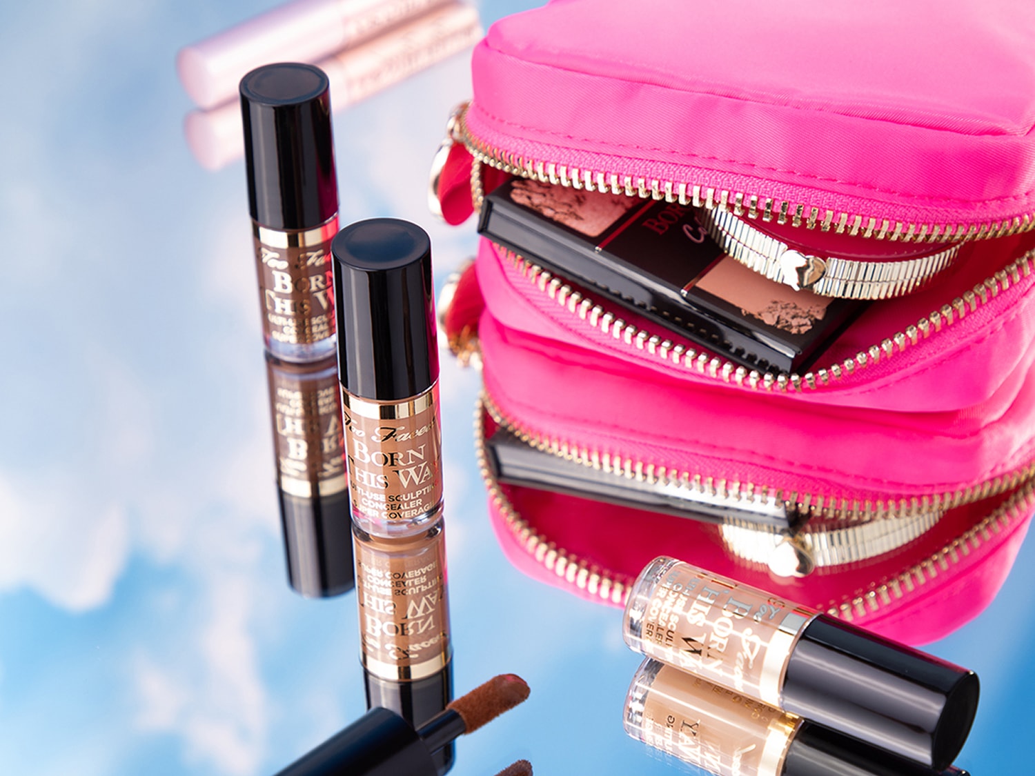 Découvrez le correcteur multi-usage Born This Way de Too Faced, idéal pour sculpter et camoufler, présenté à côté d'une trousse de maquillage rose vif.