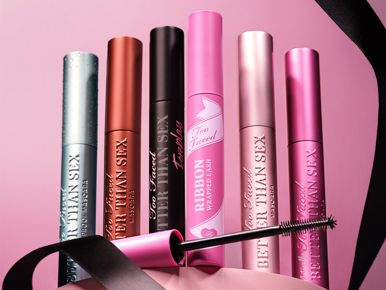 Découvrez la gamme de mascaras Too Faced Better Than Sex, avec des teintes allant du bleu argenté au rose, présentés sur un fond rose doux.