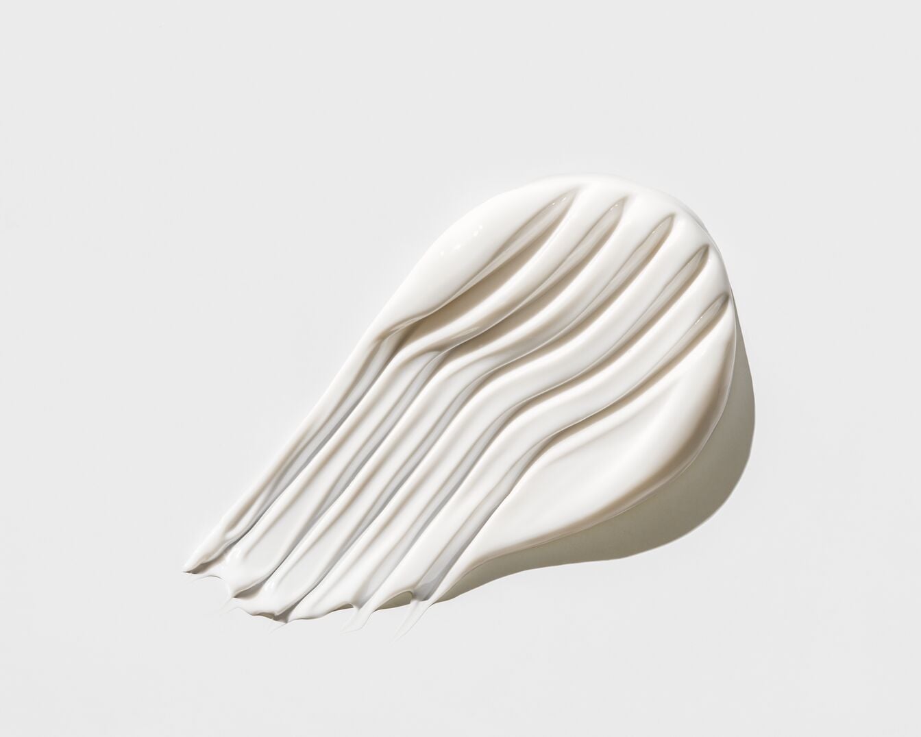 Nahaufnahme eines cremefarbenen Kosmetikprodukts mit glatter Textur, das in Streifen aufgetragen wurde und sich ideal für die Hautpflege eignet.