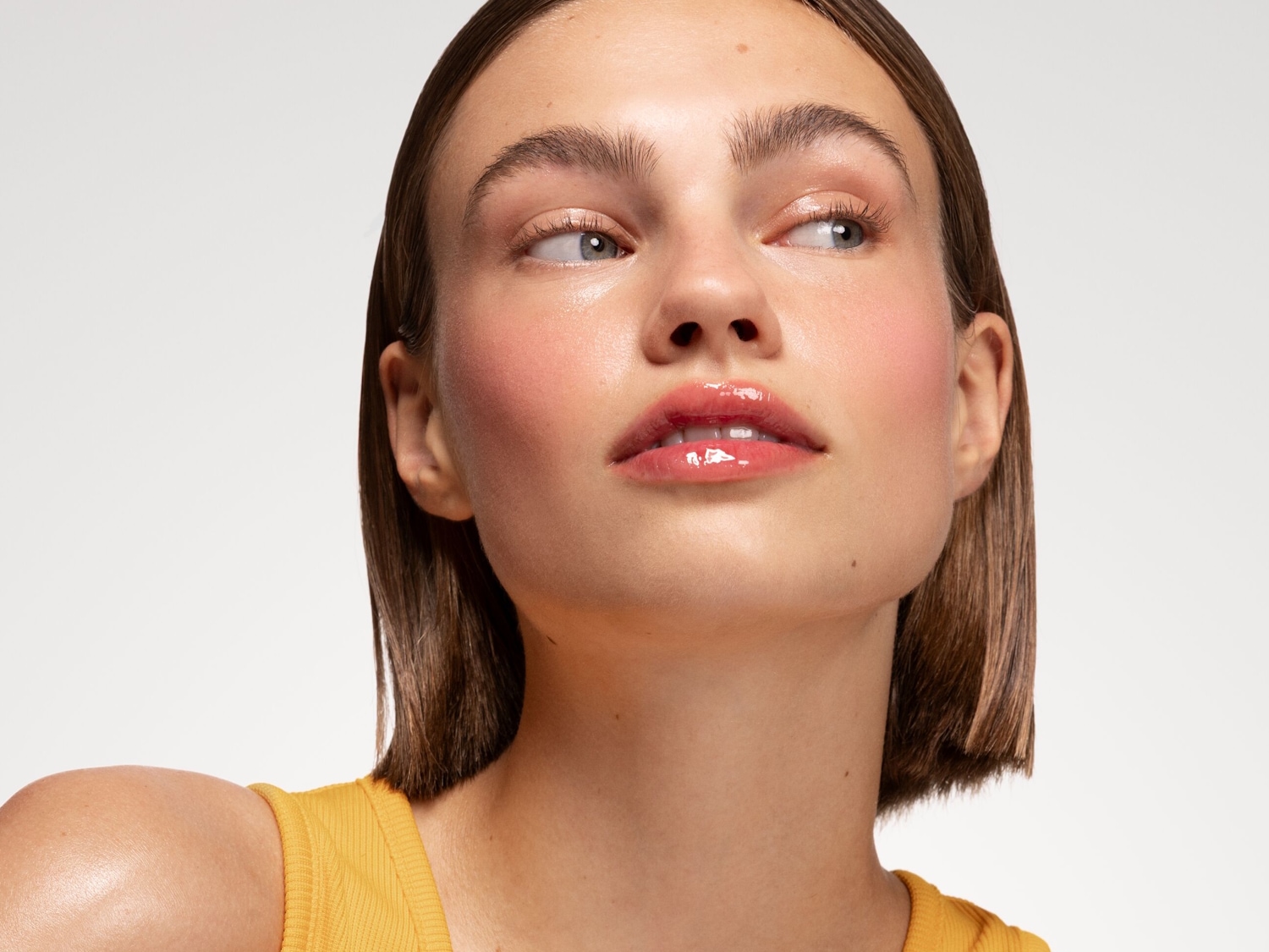 Gros plan sur un visage féminin avec un maquillage frais : joues rosées, lèvres brillantes et regard lumineux, le tout rehaussé par un teint éclatant.