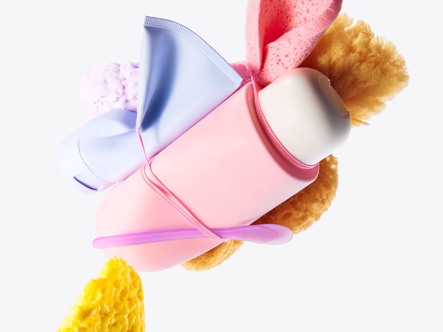 Una colección de productos de belleza, que incluye un tubo azul claro, un desodorante rosa y esponjas de diferentes colores, todo ello sobre un fondo blanco.