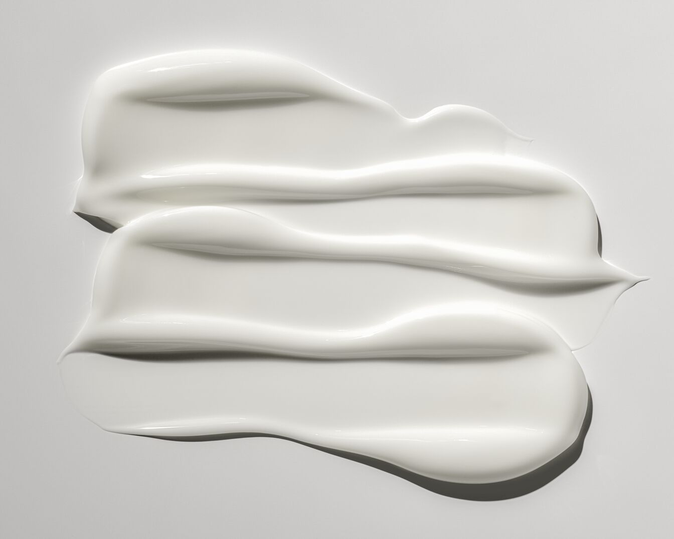 Nahaufnahme von drei glänzenden, weißen Creme- oder Lotionstrichen, die eine glatte und feuchtigkeitsspendende Textur zeigen.