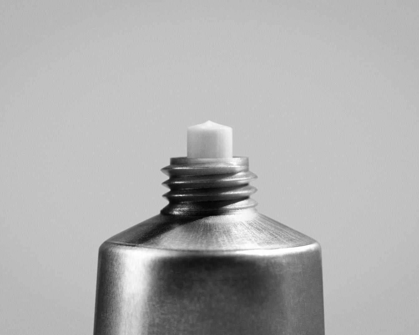 Close-up van een zilverkleurige tube met een witte, puntige opening, klaar voor gebruik.