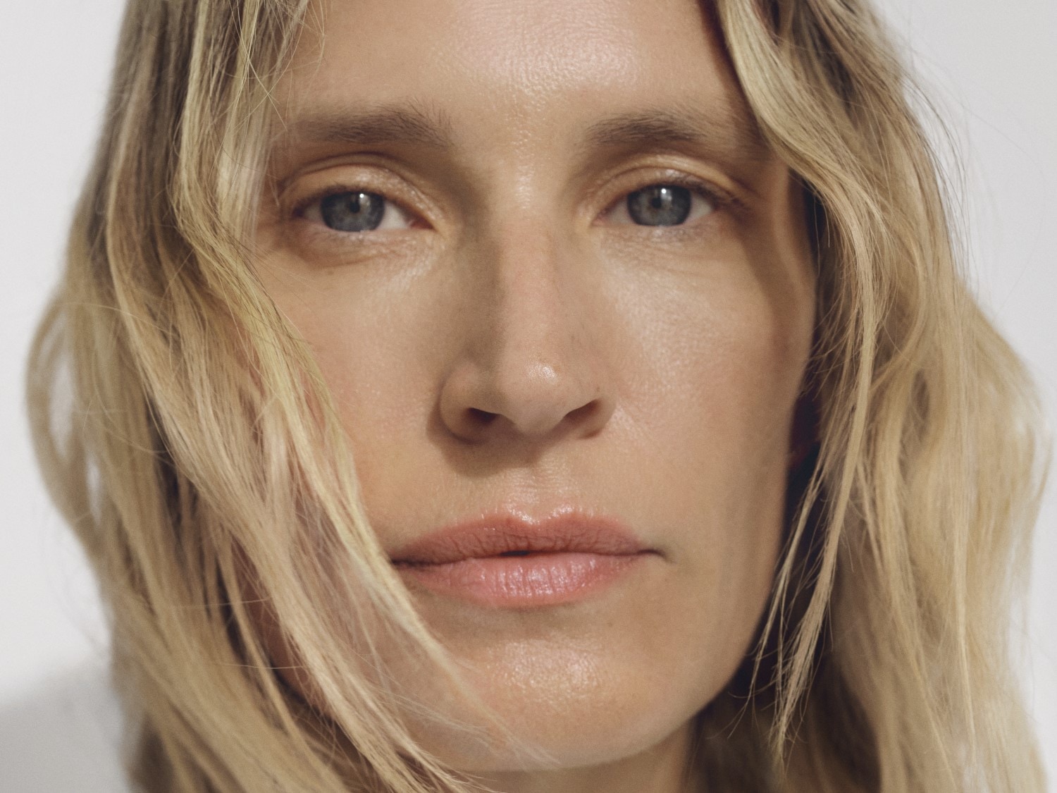 Een close-up van een vrouw met blond haar en blauwe ogen, haar huid heeft een natuurlijke glans en haar lippen zijn lichtroze.