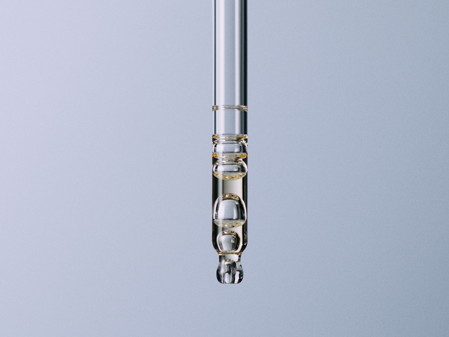Close-up van een glazen pipet gevuld met een heldere, gouden vloeistof, perfect voor het doseren van serums of oliën.