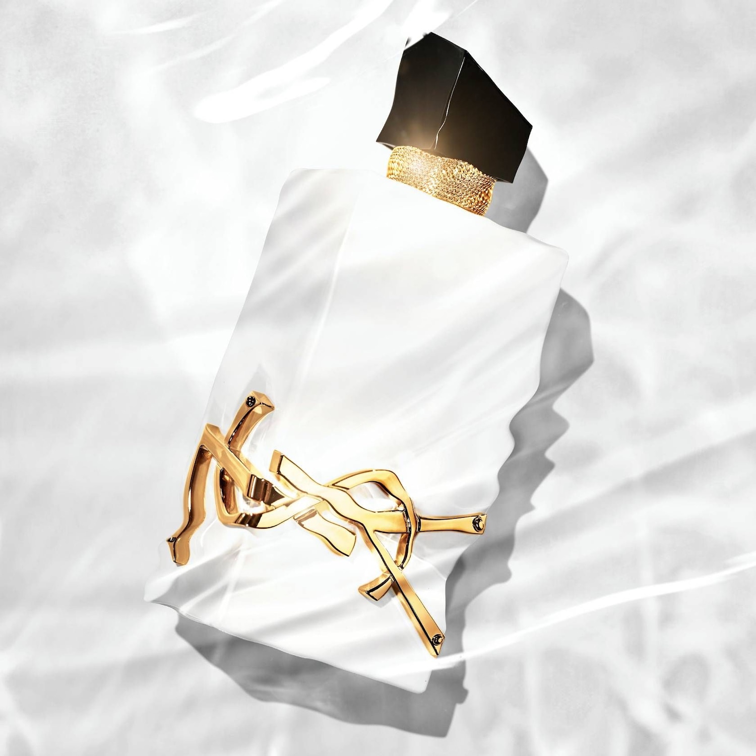A fehér YSL Libre Eau de Parfum üvegén arany színű logó látható, fekete kupakkal és arany nyaklánccal.
