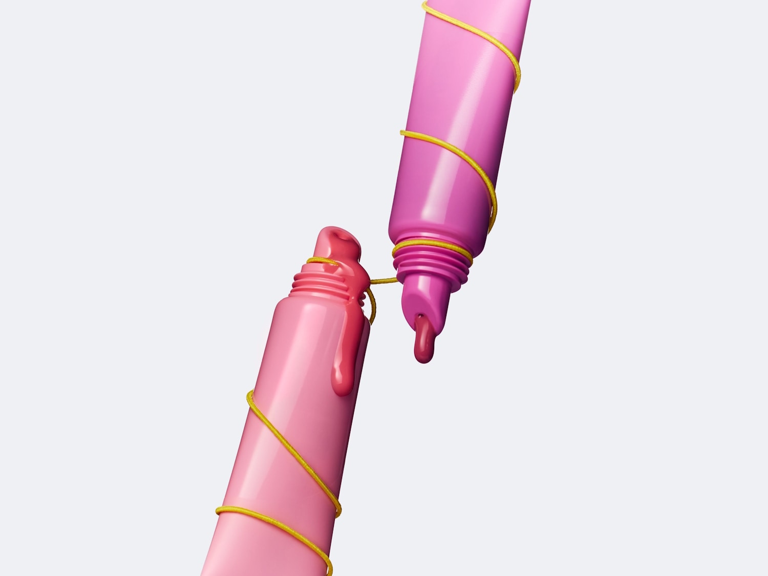 Zwei rosa Farbtuben sind mit gelbem Faden umwickelt, aus einer Tube tropft rosa Farbe, was einen verspielten und kreativen Eindruck erweckt.