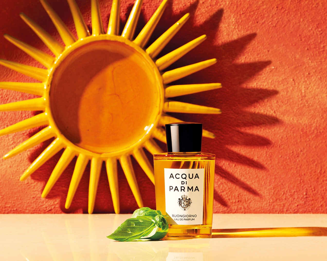 Sluneční dekorace a flakon parfému Acqua di Parma Buongiorno Eau de Parfum s bazalkovými lístky.