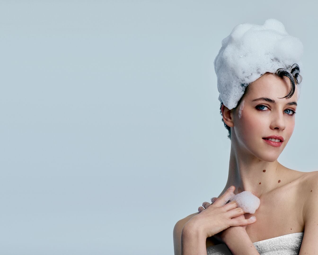 Nahaufnahme von dunklem, nassem Haar, auf das eine dicke, weiße Spülung aufgetragen wird, die an den Strähnen herunterläuft.