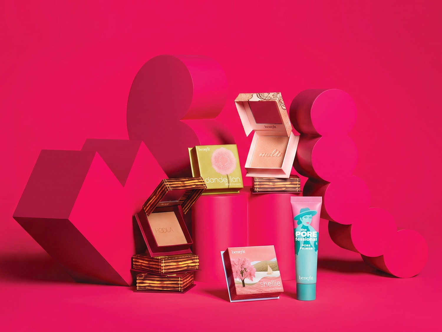 Een levendige roze achtergrond met verschillende Benefit Cosmetics producten, waaronder blushes, bronzers en primers, die een speelse en kleurrijke make-upcollectie presenteren.
