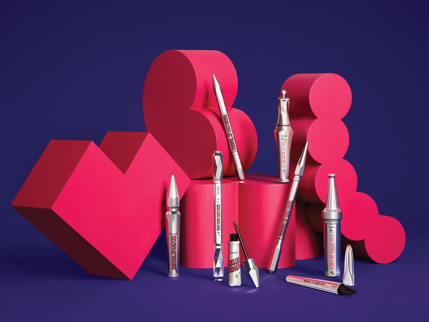 Een assortiment van Benefit Cosmetics wenkbrauwproducten, waaronder potloden, gels en waxen, staat op roze hartvormige en ronde platforms tegen een donkerblauwe achtergrond.