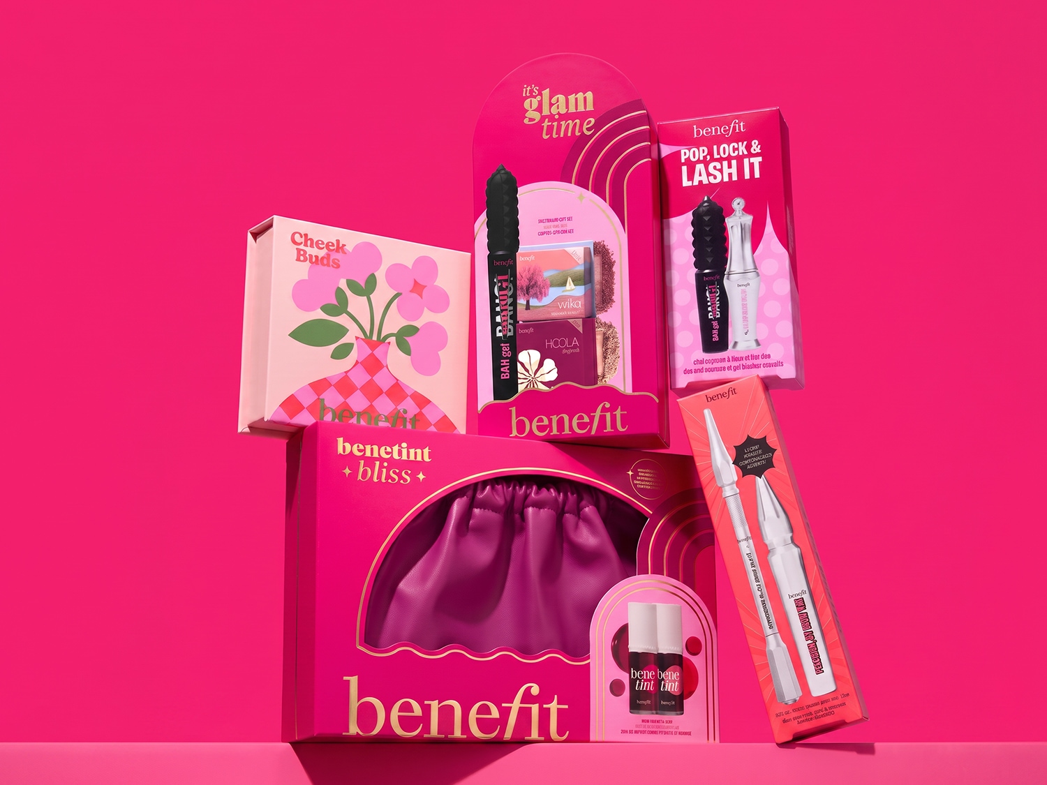 Een levendige collectie Benefit make-up geschenksets, waaronder de "Cheek Buds" blush, "Benetint + Bliss" lip- en wangtint, "Pop, Lock & Lash It" mascara en wenkbrauwproducten, allemaal gepresenteerd op een felroze achtergrond.