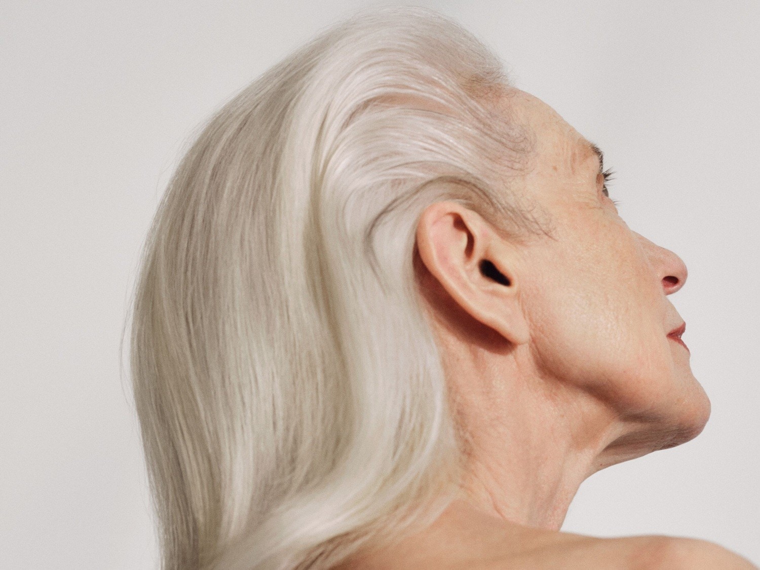 Profiel van een vrouw met golvend wit haar, een subtiele rode lippenstift en een klein zwart oordopje in haar oor.