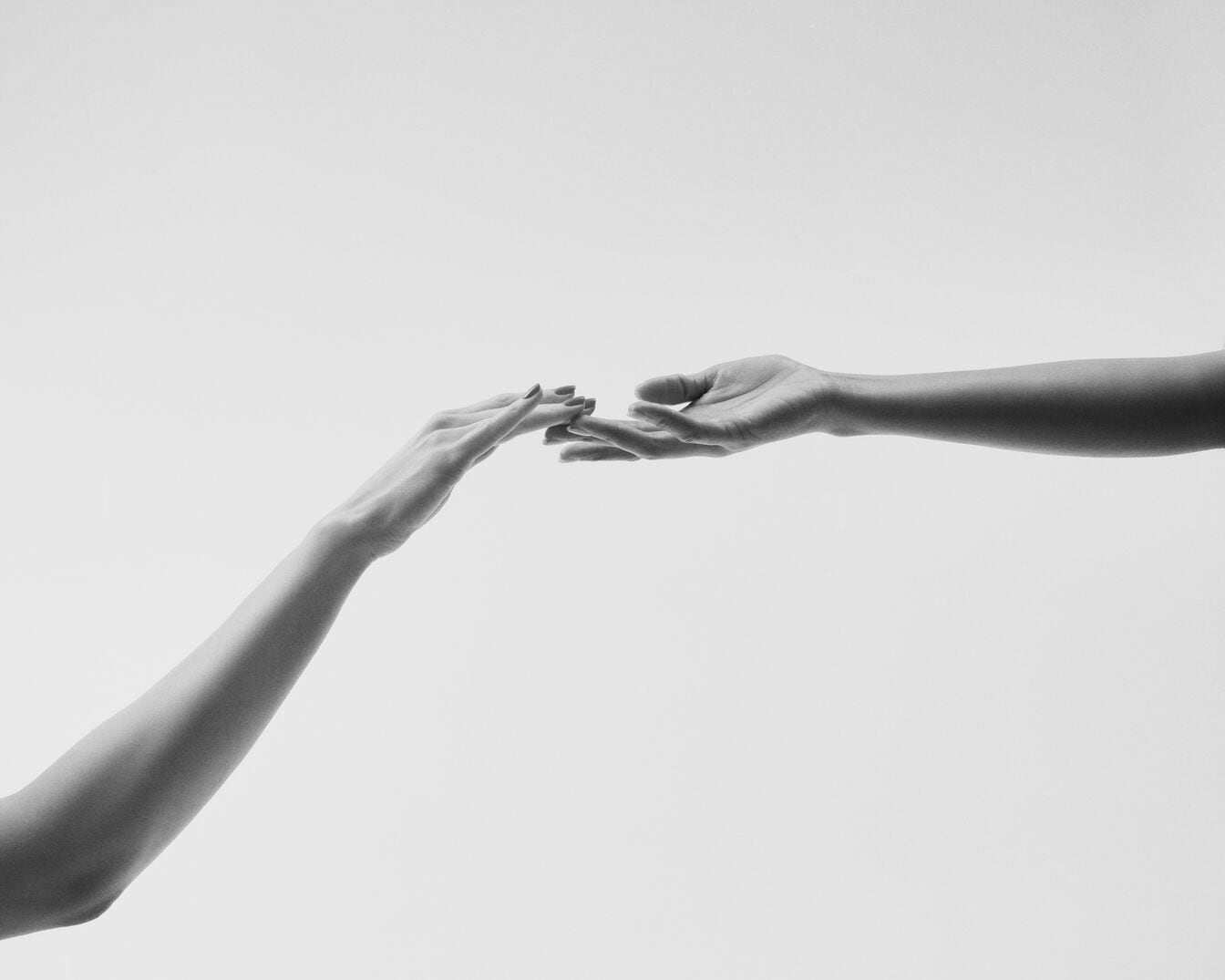 In zwart-wit, twee handen reiken naar elkaar toe tegen een heldere achtergrond, een delicate aanraking suggereert verbinding en intimiteit.