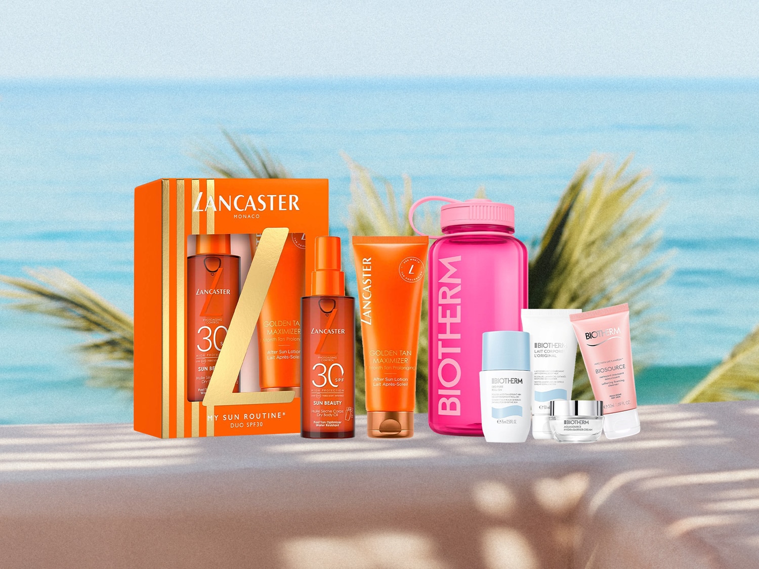 Un coffret Lancaster Monaco "My Sun Routine" Duo SPF30, comprenant une huile sèche corps et un lait après-soleil, est présenté à côté d'une bouteille d'eau rose Biotherm et de plusieurs produits de soin Biotherm, le tout sur fond de mer bleue et de palmiers.