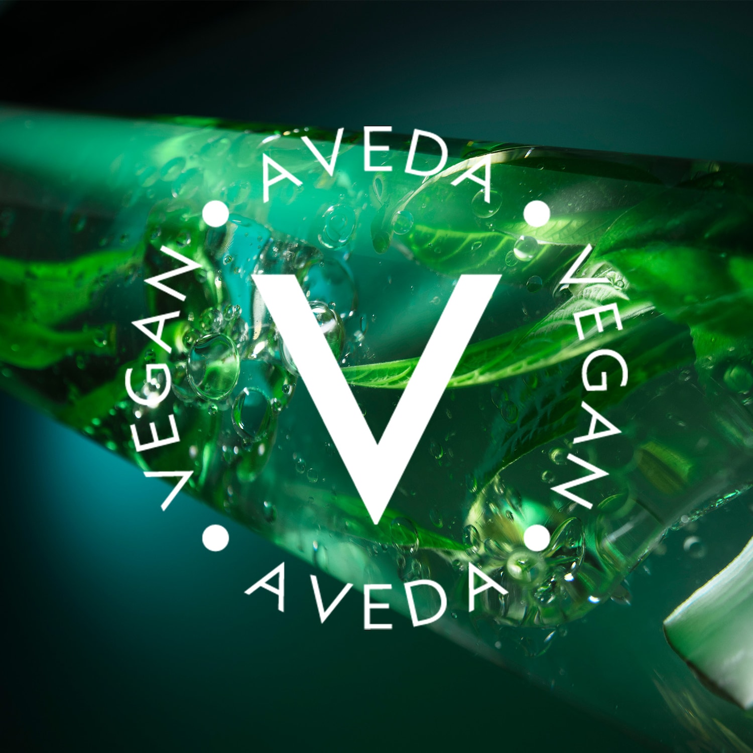 Nahaufnahme einer transparenten, grünen Flüssigkeit mit Blättern und Luftblasen, umgeben von einem weißen Kreis mit der Aufschrift AVEDA VEGAN.