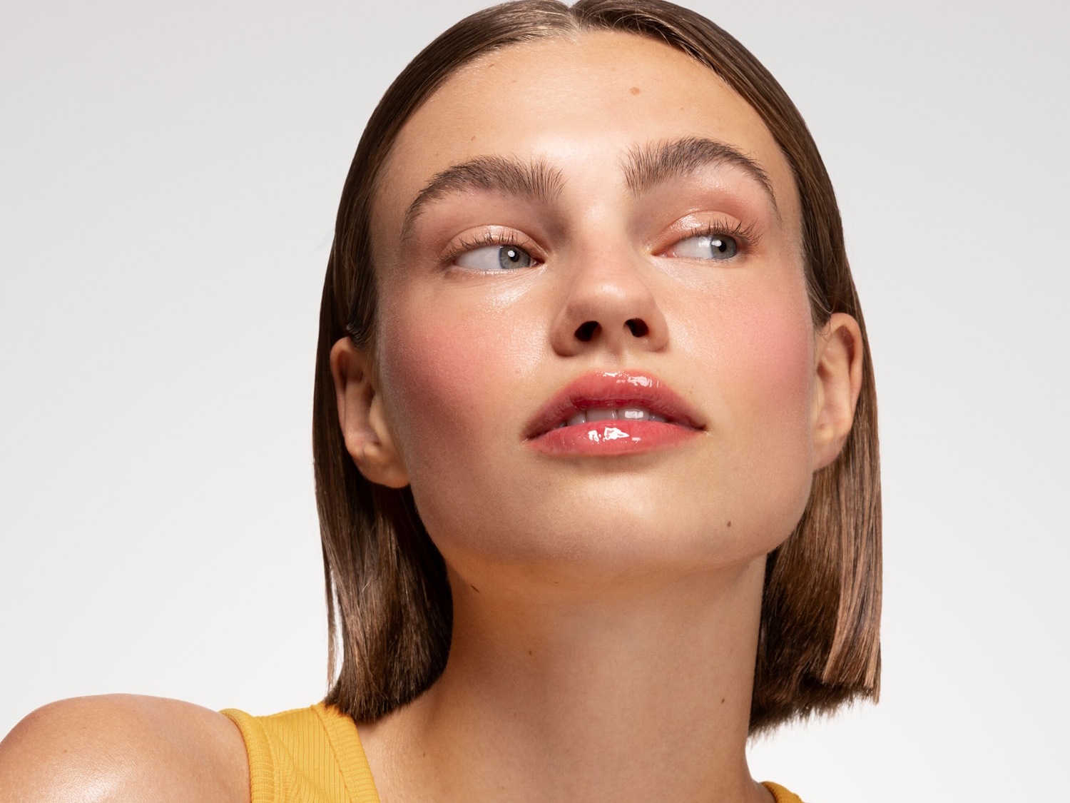Nahaufnahme eines Models mit glänzenden Lippen und rosigem Rouge, das einen frischen, strahlenden Look präsentiert.