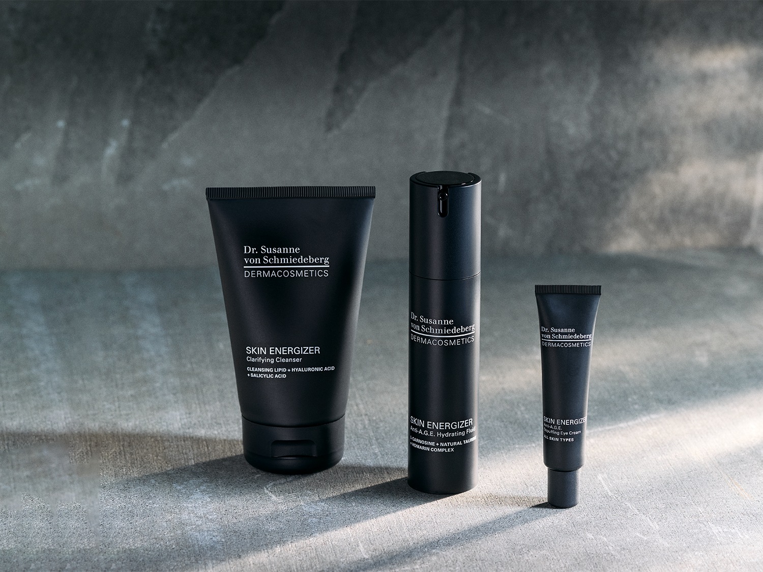 Voici un ensemble de soins pour la peau Dr. Susanne von Schmiedeberg, comprenant un nettoyant clarifiant, un fluide hydratant anti-âge et une crème contour des yeux, tous présentés dans un élégant emballage noir.