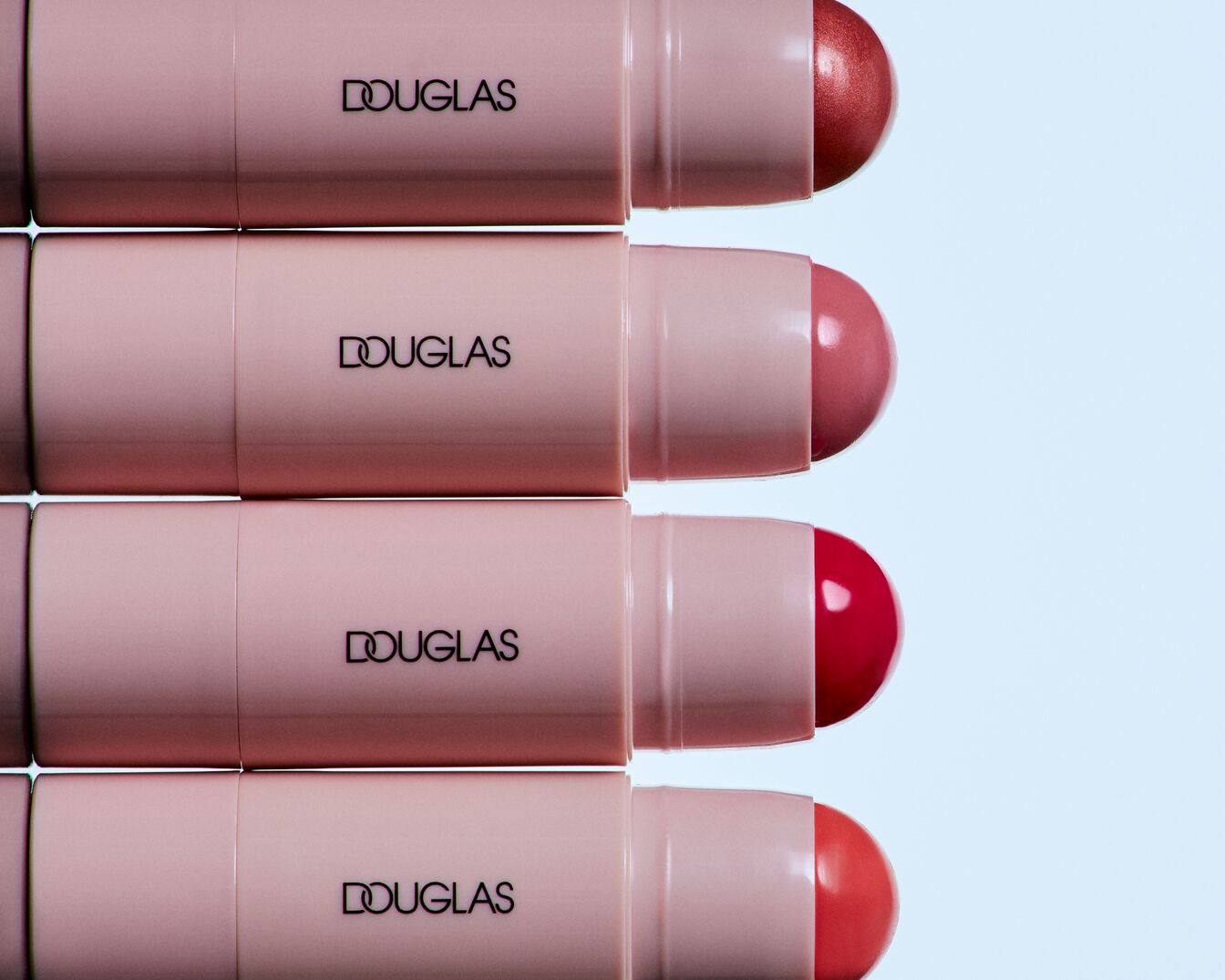 Nahaufnahme von Douglas Lippenstiften in verschiedenen Rottönen, die in einer Reihe angeordnet sind und deren Verpackung ein zartes Rosa aufweist.