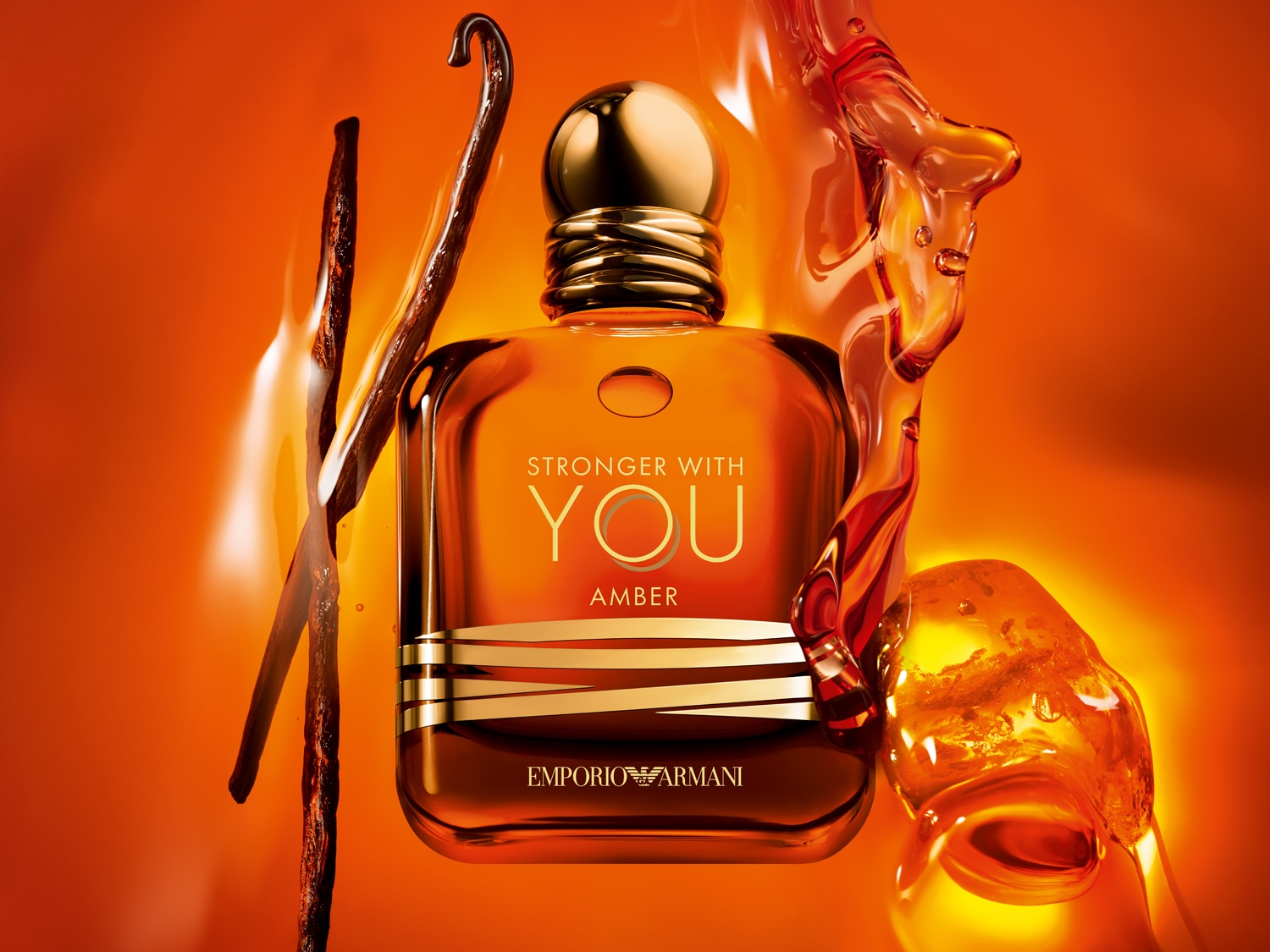 Az Emporio Armani Stronger With You Amber üvegben, arany kupakkal és csíkokkal, vaníliarúddal és borostyánszínű folyadékkal körülvéve.