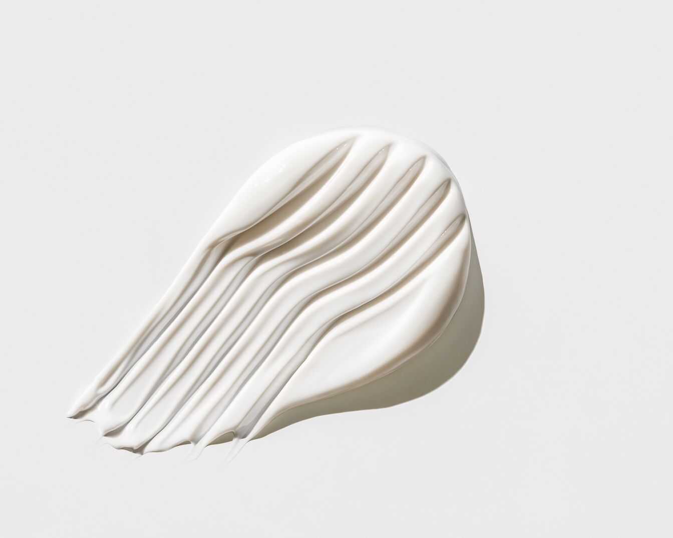 Een close-up van een witte crème uitgesmeerd op een witte achtergrond, de textuur is glad en glanzend.