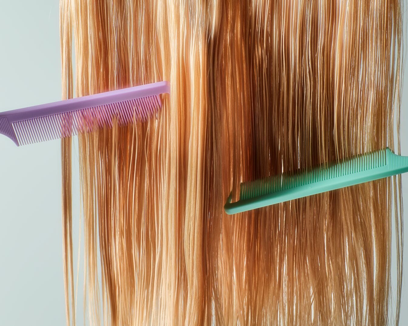 Nahaufnahme von glattem, blondem Haar, das mit einem lila und einem grünen Kamm gekämmt wird.