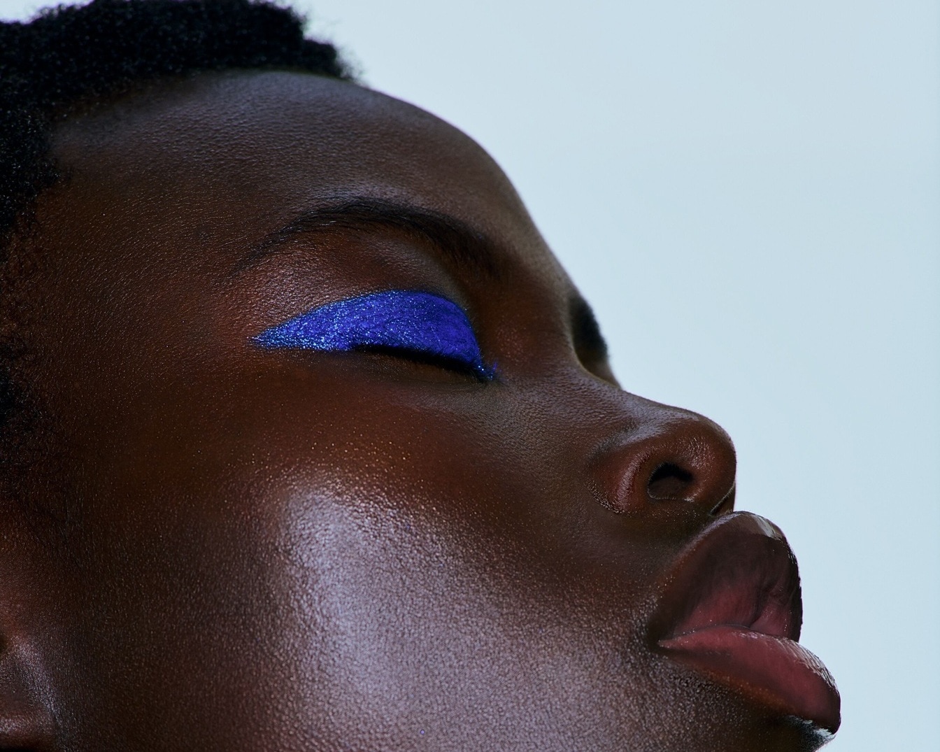 Nahaufnahme eines dunkelhäutigen Models mit geschlossenem Auge und blauem, glitzerndem Eyeliner, der einen auffälligen Akzent setzt.