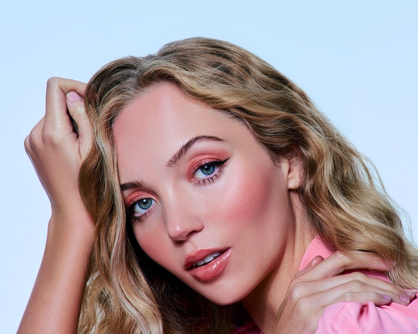 Nahaufnahme einer Frau mit blonden, gewellten Haaren, zartem rosa Make-up auf Augen und Wangen und glänzenden Lippen, die einen femininen und frischen Look kreiert.