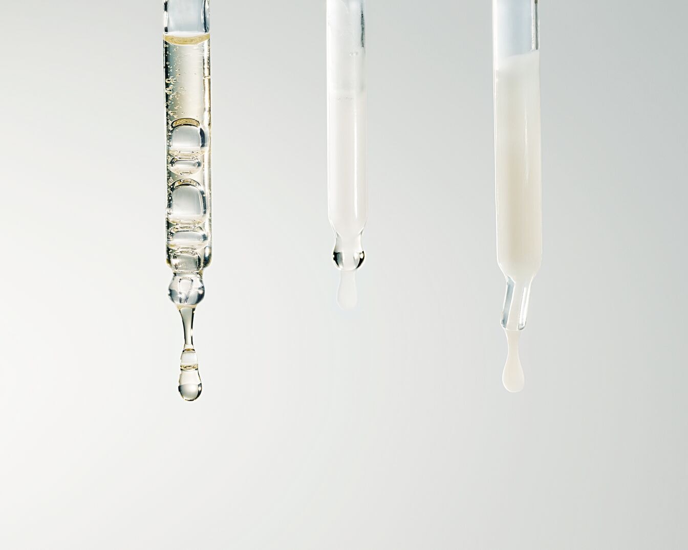 Drie glazen pipetten gevuld met heldere en witte vloeistoffen, klaar om de huid te hydrateren en te voeden.