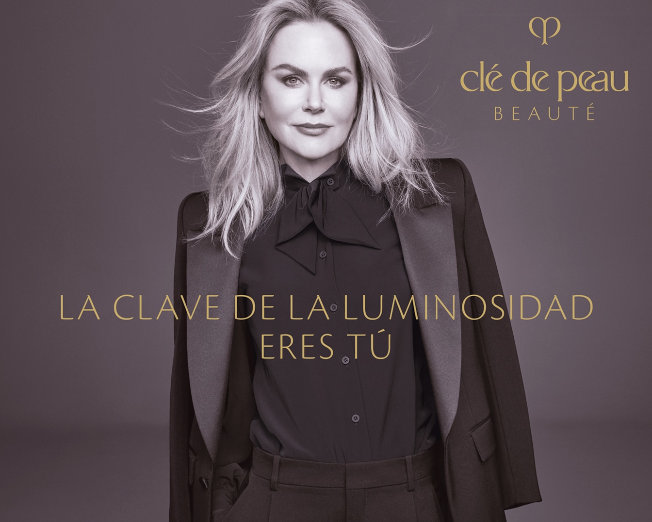 La imagen muestra a Nicole Kidman con un blazer negro y una blusa con lazo, junto al logo de Clé de Peau Beauté y el texto dorado "LA CLAVE DE LA LUMINOSIDAD ERES TÚ".