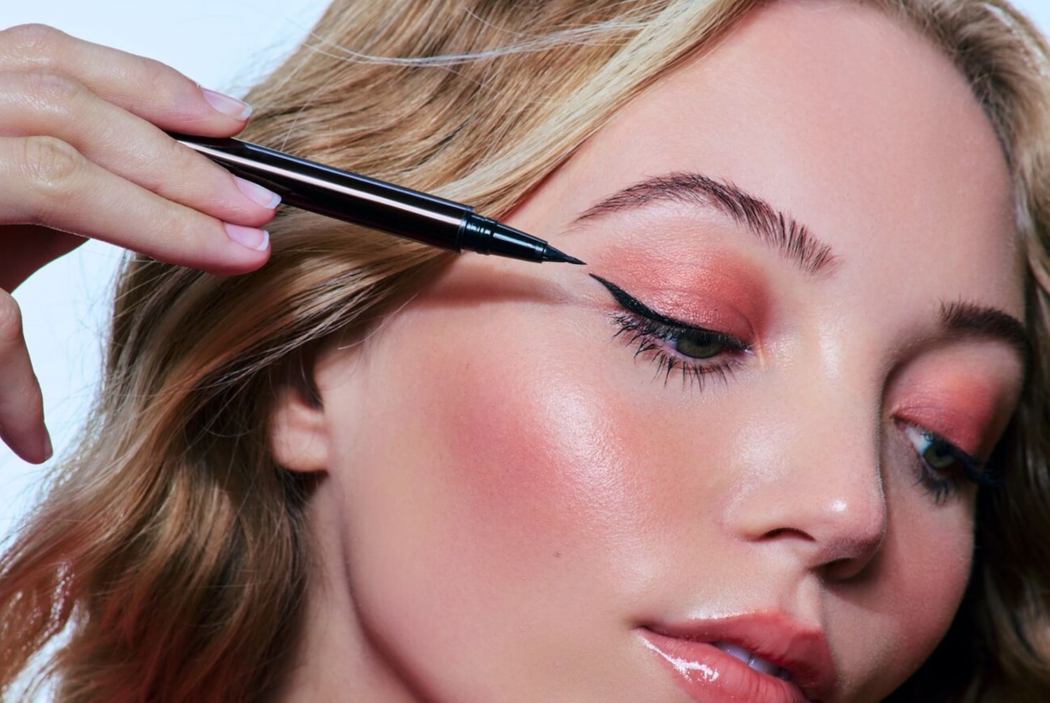 Une femme blonde applique un eye-liner noir avec un applicateur fin pour créer un regard défini et élégant.