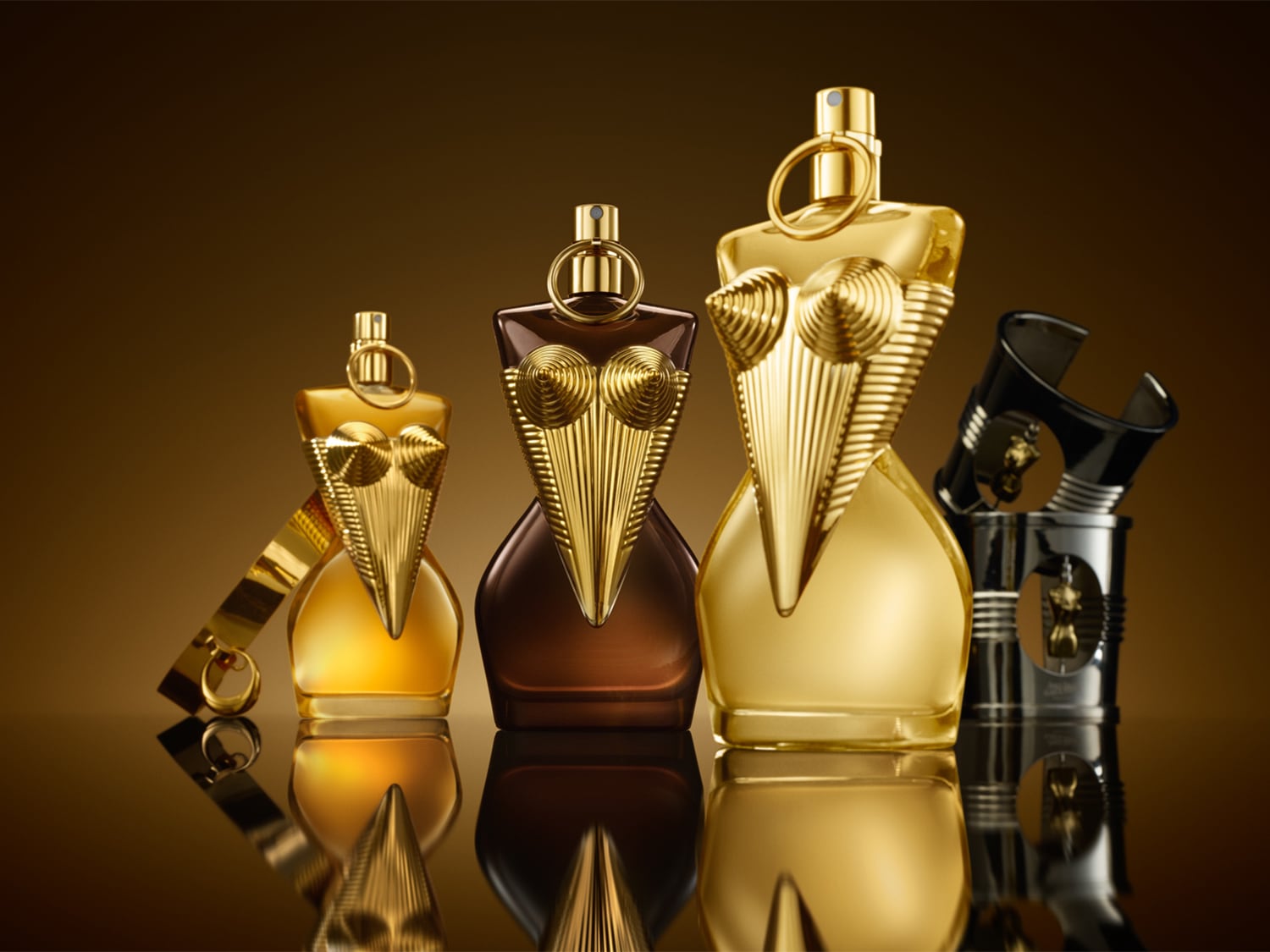 Gouden parfumflessen in de vorm van een vrouwelijk torso, variërend in grootte en tinten goud en bruin, staan op een glanzend oppervlak.