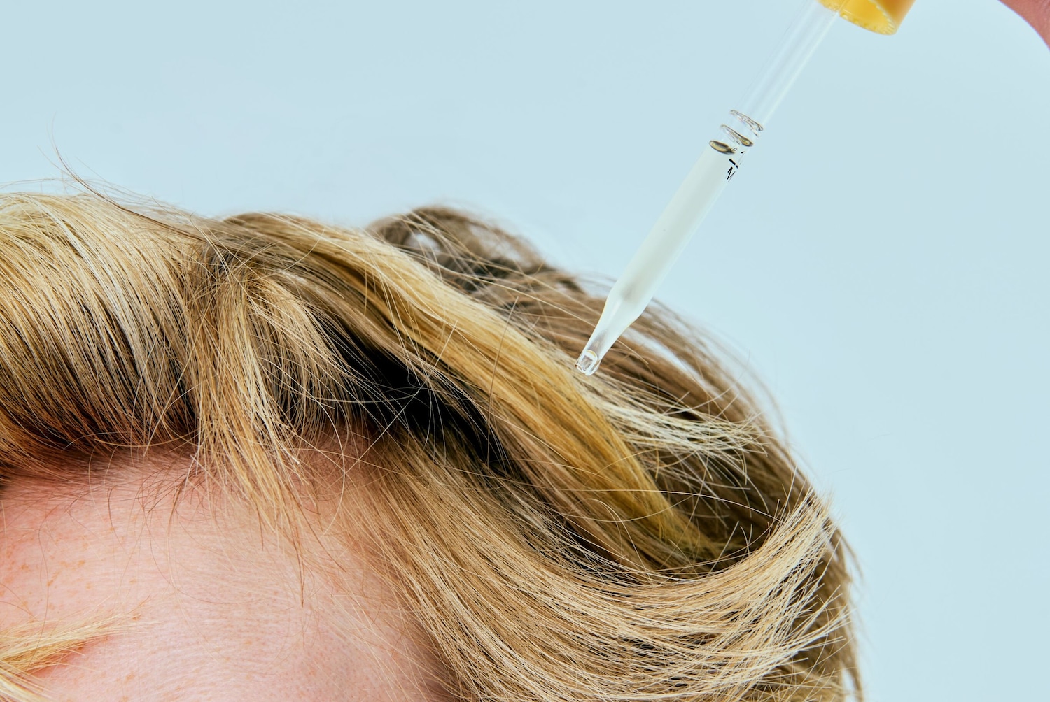 Nahaufnahme von blondem Haar, auf das mit einer Pipette ein Serum aufgetragen wird, um die Haargesundheit zu verbessern.