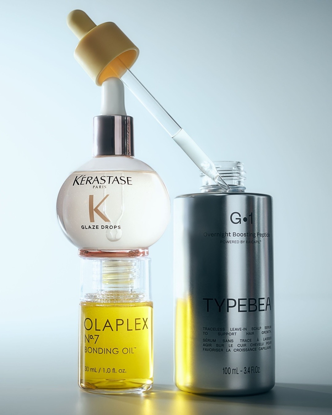 Tři lahvičky vlasových sér od Kérastase, Olaplex a Typebea, které slibují posílení a růst vlasů, s pipetami pro snadnou aplikaci.