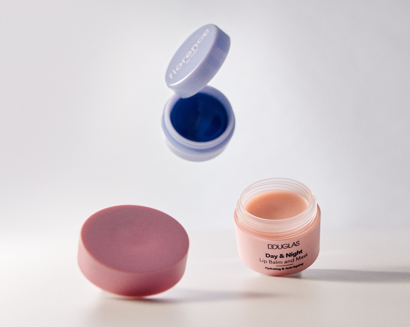 Zwei Lippenpflegeprodukte von Douglas und Florence: Der Douglas Day & Night Lippenbalsam in einer rosa Dose und die Florence Lippenmaske in einer lila Dose.
