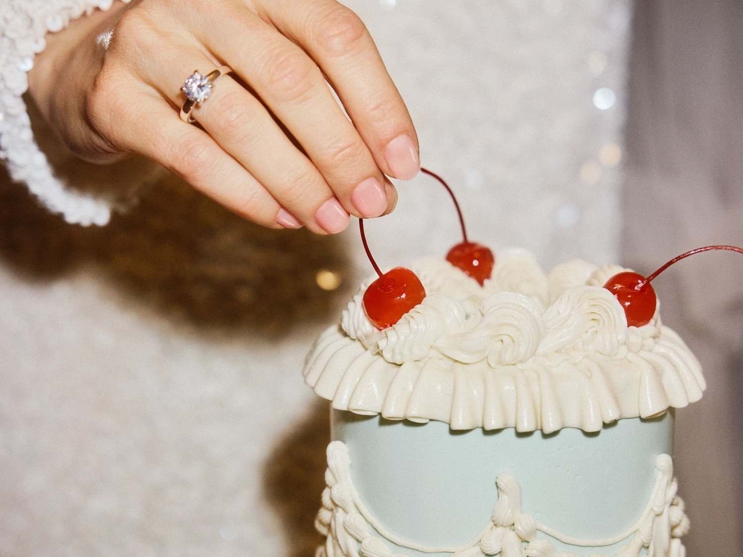 Rankos pirštas su žiedu deda vyšnią ant torto su baltu kremu ir raudonomis vyšniomis.