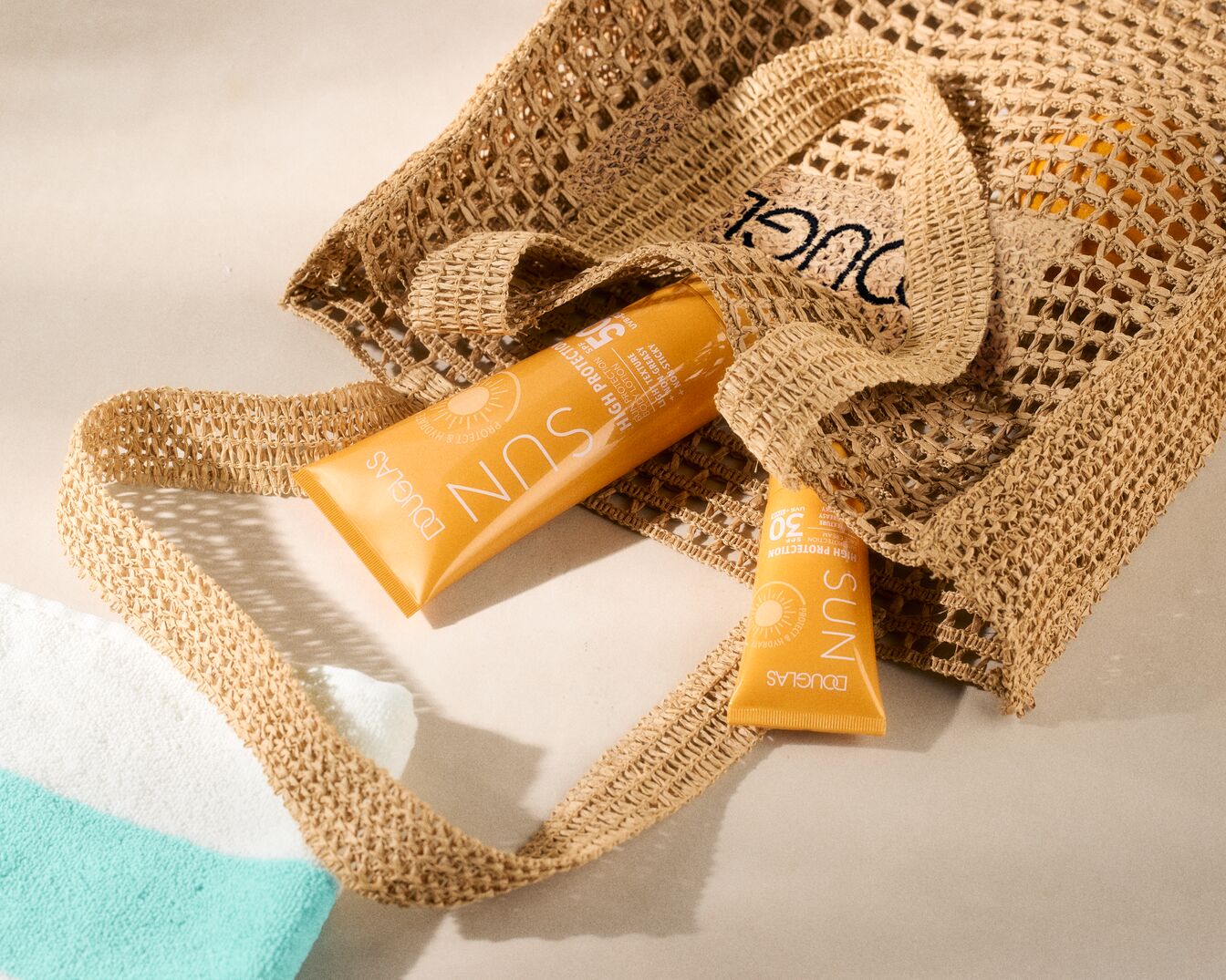 Torba plażowa z filtrem przeciwsłonecznym Douglas Sun SPF 50 i SPF 30 w pomarańczowych tubkach, zapewniająca wysoką ochronę.