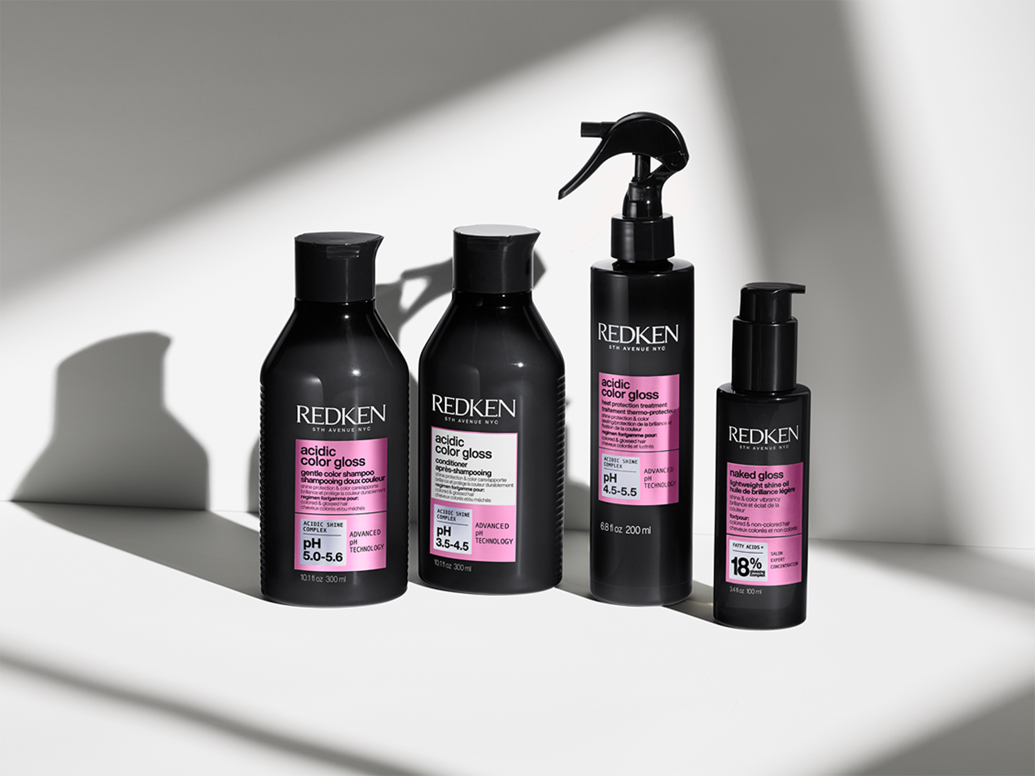 Vier zwarte flessen Redken Acidic Color Gloss haarverzorgingsproducten, waaronder shampoo, conditioner, hittebescherming en naked gloss olie.