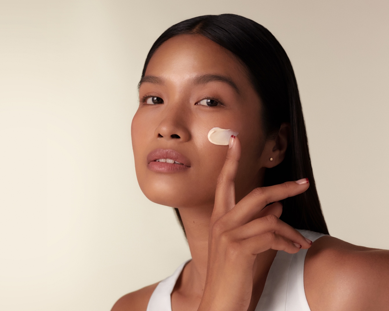 Primo piano di una donna che applica una crema color carne sulla guancia con un dito, incarnando una routine di bellezza e cura della pelle.