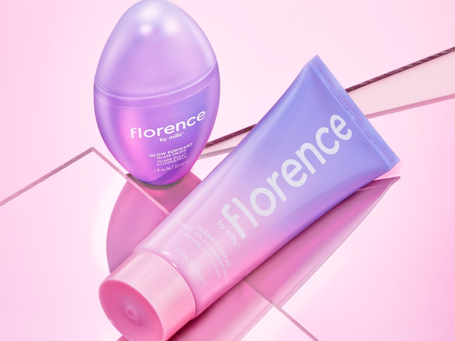 „Florence by Mills“ kosmetikos rinkinys su „Glow Forward Glaze Drops“ ir „Clear Canvas Milky Oil Cleansing Balm“ švelniai violetiniuose buteliukuose, skirtas odai spindėti.