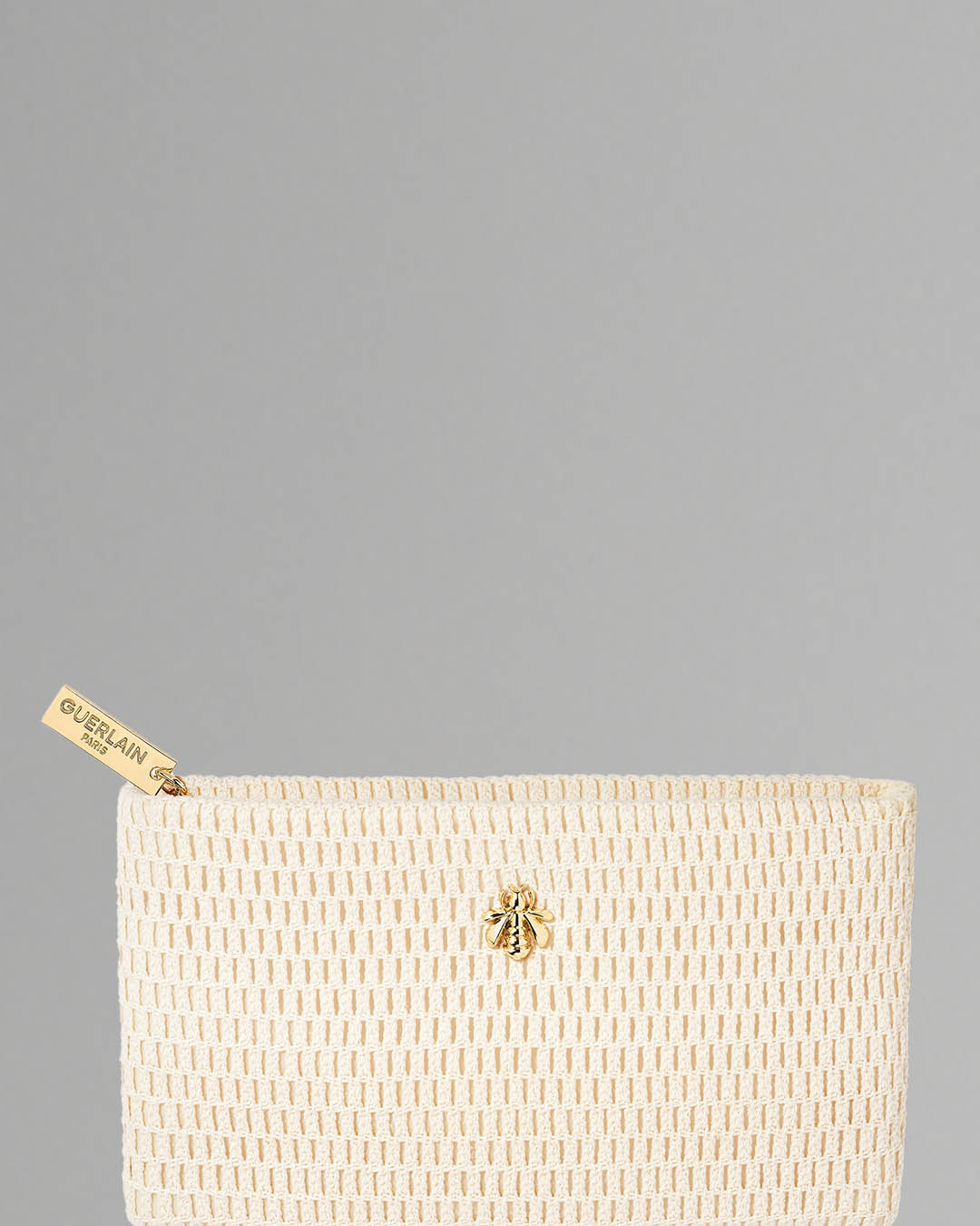 Kremowa, tkana kosmetyczka z logo Guerlain na suwaku i złotą pszczołą, idealna do przechowywania ulubionych kosmetyków.