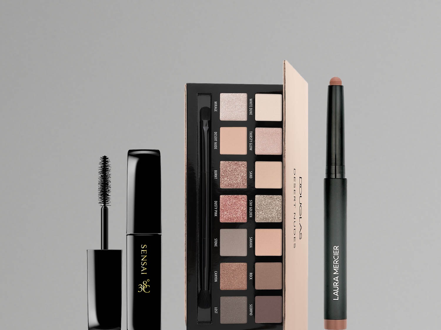 Zestaw kosmetyków do makijażu oczu, w skład którego wchodzą tusz do rzęs Sensai w czarnym opakowaniu, paleta cieni do powiek Douglas Desert Nudes z różnorodnymi odcieniami oraz szminka Laura Mercier w sztyfcie.